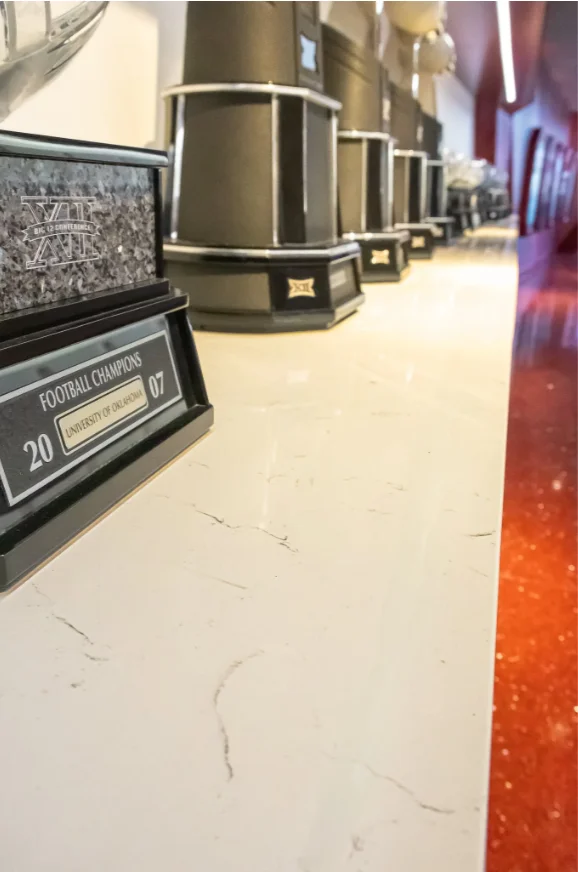 Light stone countertop displaying University of Oklahoma football trophies, showing the surface finish and subtle veining