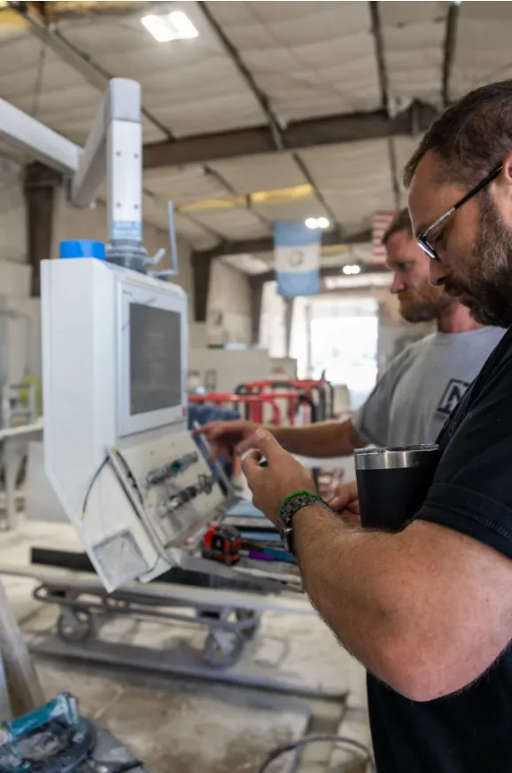 Two TNT Countertops team members reviewing a slab layout on a CNC machine control panel in the fabrication shop