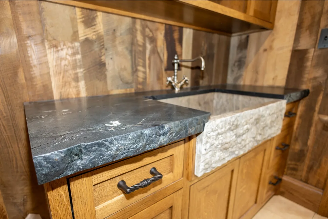 Dark stone countertop with rustic chiseled farmhouse sink in a warm wood kitchen