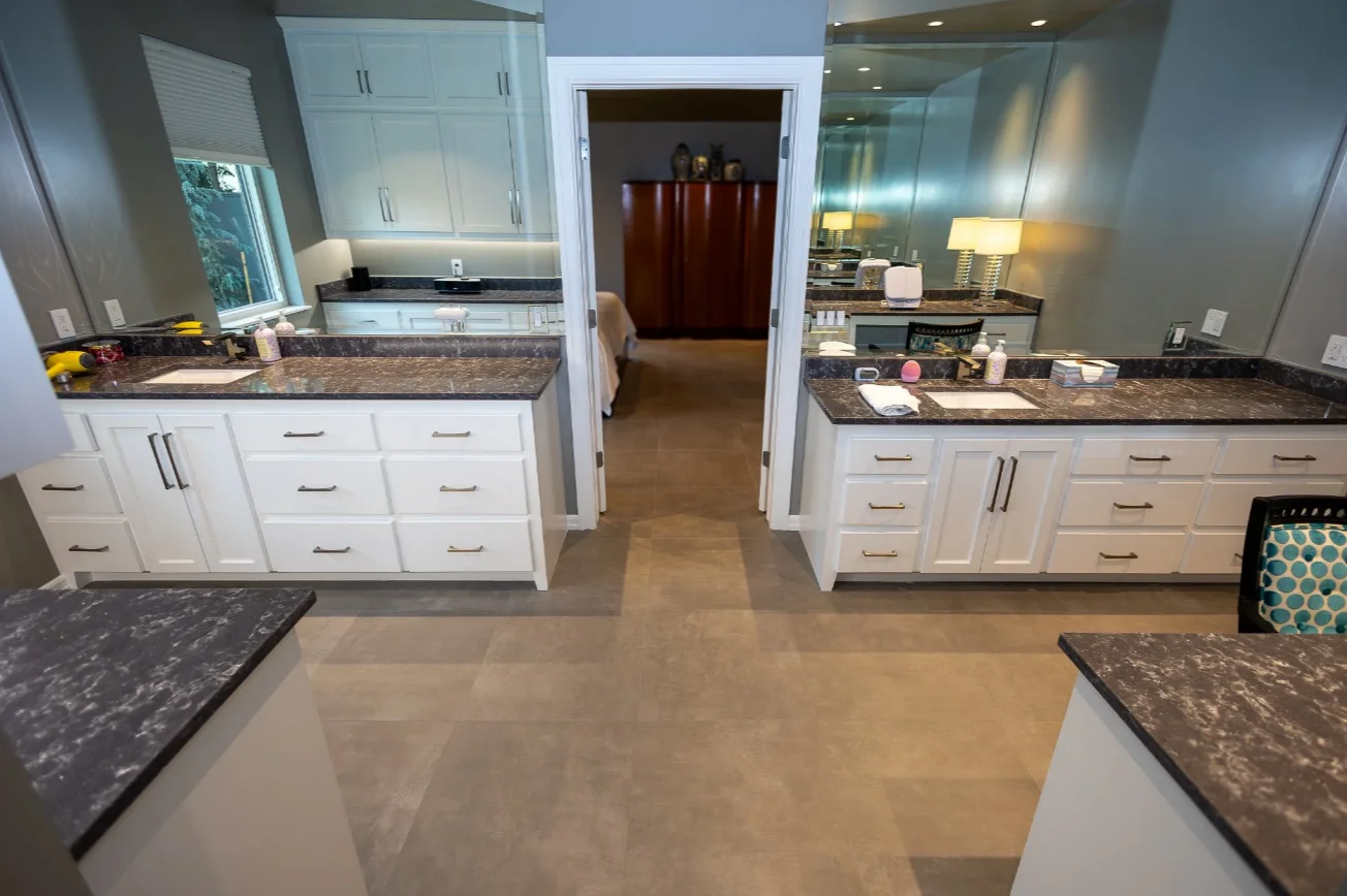 Bathroom with dark stone countertops, white vanity cabinetry, and large mirrors